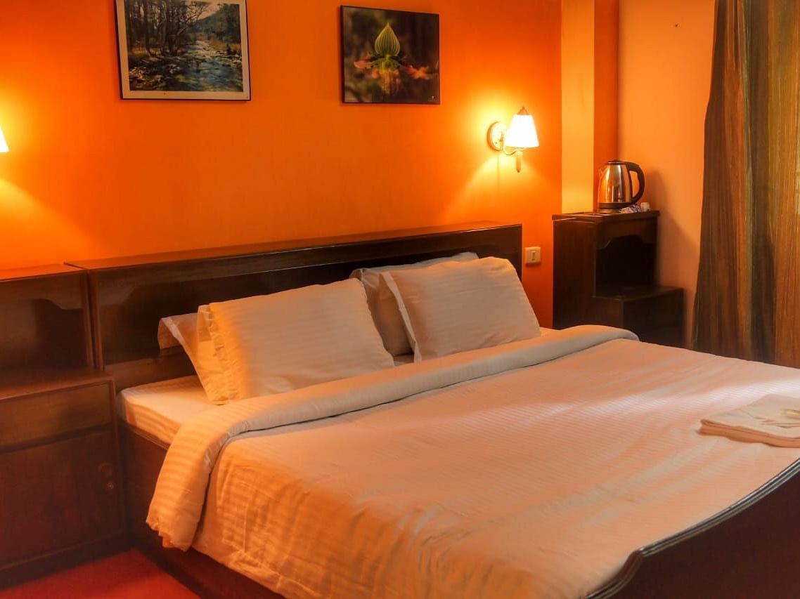 An image of the deluxe room featuring a queen size bed, bed side table, lamps, and painting hung on the wall - Ecotel Chiminda, Pelling