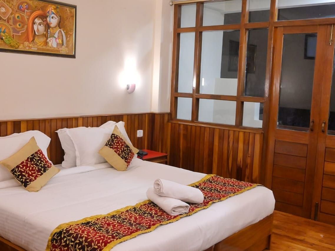 An image of the super deluxe room featuring a queen size bed, bed side table, lamps, and an expansive door leading to the balcony - Ecotel Chiminda, Pelling