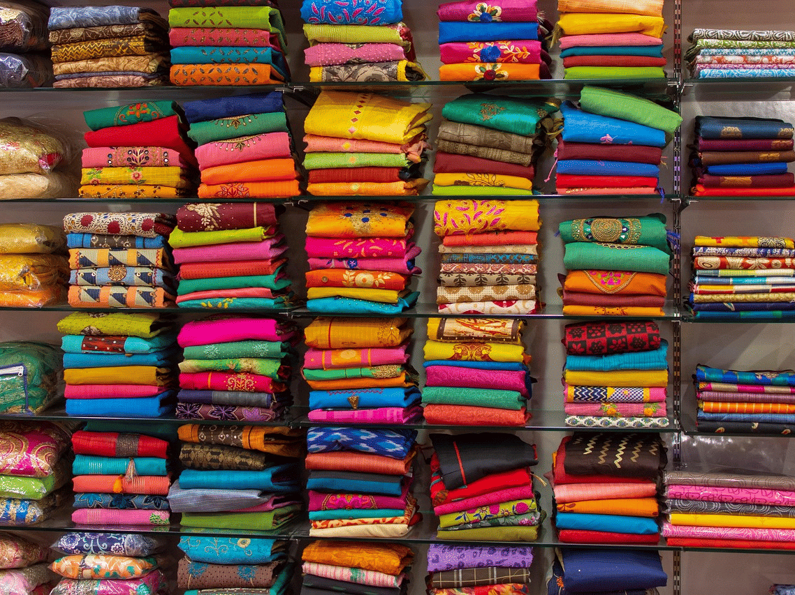 A shop with a shelf, full of different garments, on display.