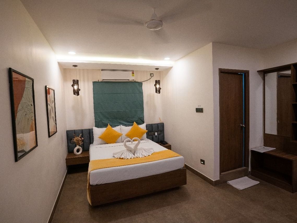 A room with a double bed, decorative pillows, wall art, and warm lighting, offering a welcoming atmosphere at Hotel Kyzen Smartstays – Smart, Reliable, Kyzen