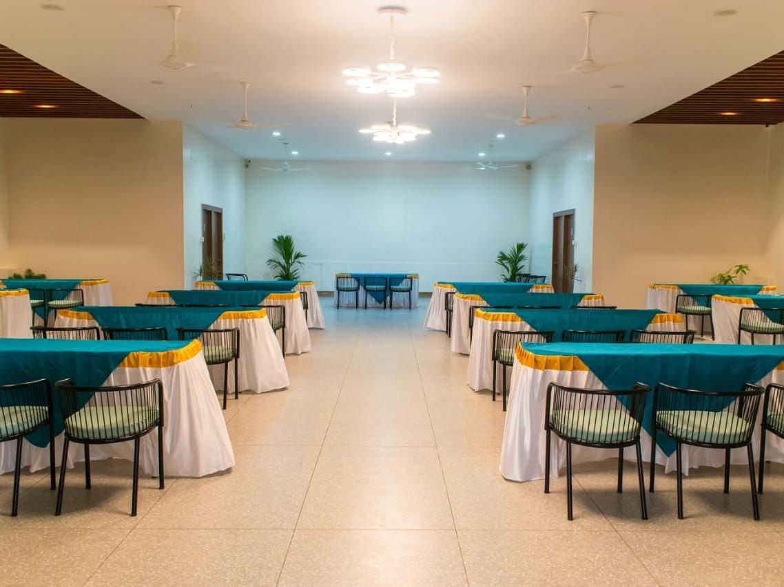 A banquet hall set up for an event with tables and turquoise table cloths - Lords Eco Inn Belagavi