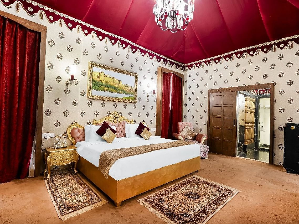 Side view of a  lavishly decorated tent suite at the Rajasthali Resort & Spa in Jaipur features a four-poster bed, ornate furnishings, and a red draped ceiling.