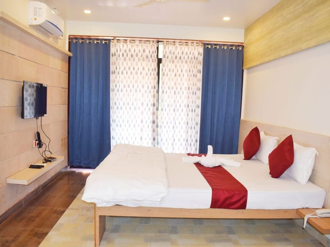 A side view of a spacious room with a large bed. Right opposite to it, there is a wall-mounted TV, and a large window with curtains fully covering it at SeaFort Beach Resort