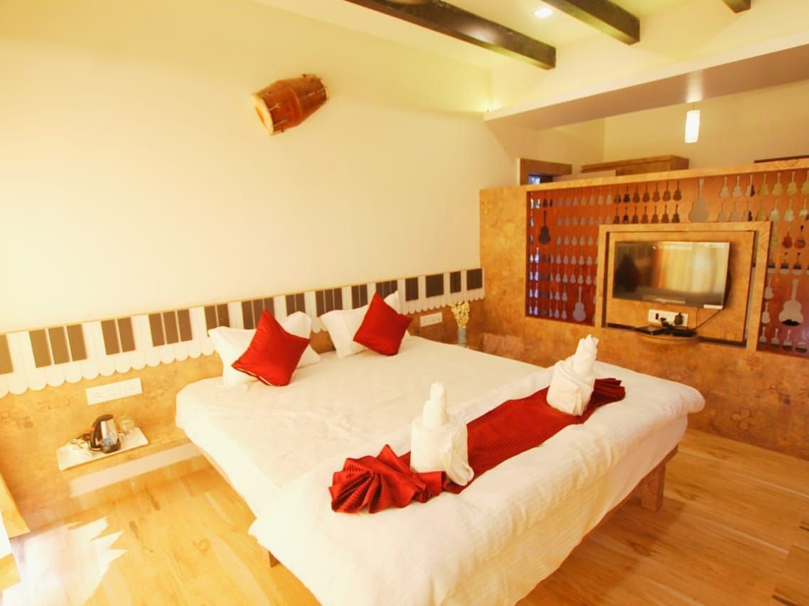 A diagonal view of the room featuring a spacious bed with towels folded in different shapes on it. There is a wooden table with a wall-mounted television at SeaFort Beach Resort