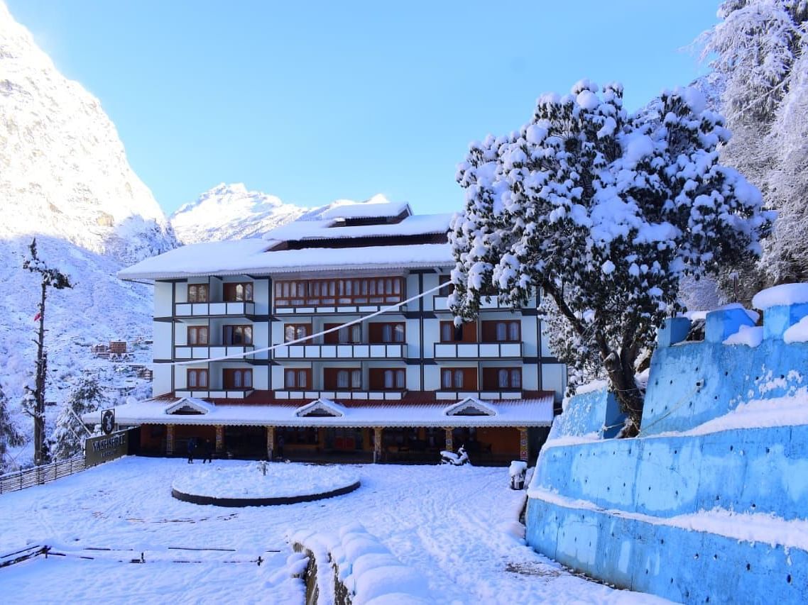 Image of the hotel covered with snow with mountains on either side and few trees   | Yashshree Lachung