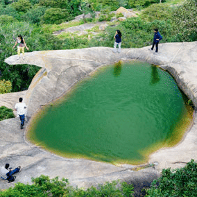 A small green-coloured lagoon on a rock platform at Avalabetta in Bengaluru, with several people surrounding it enjoying the views fro the hill top.