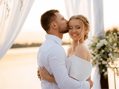 A couple in white attire shares a kiss against the backdrop of a sunlit beach, bathed in the warm glow of sunset - S Hotel Montego Bay, Jamaica
