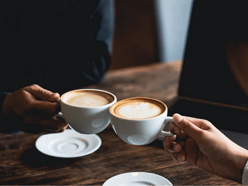 Two people clinking coffee cups in a cosy cafe - S Hotel Montego Bay, Jamaica