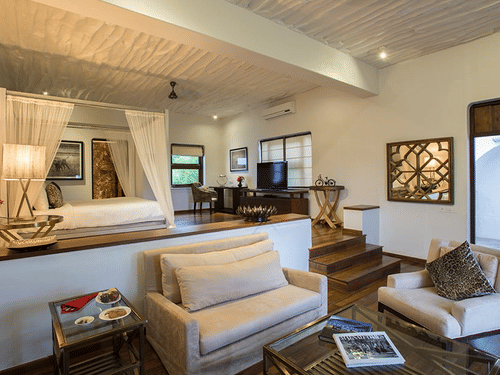 Interior of The Residence at The Serai Bandipur, featuring living space with sofas, table, wall art, and an elevated bed.