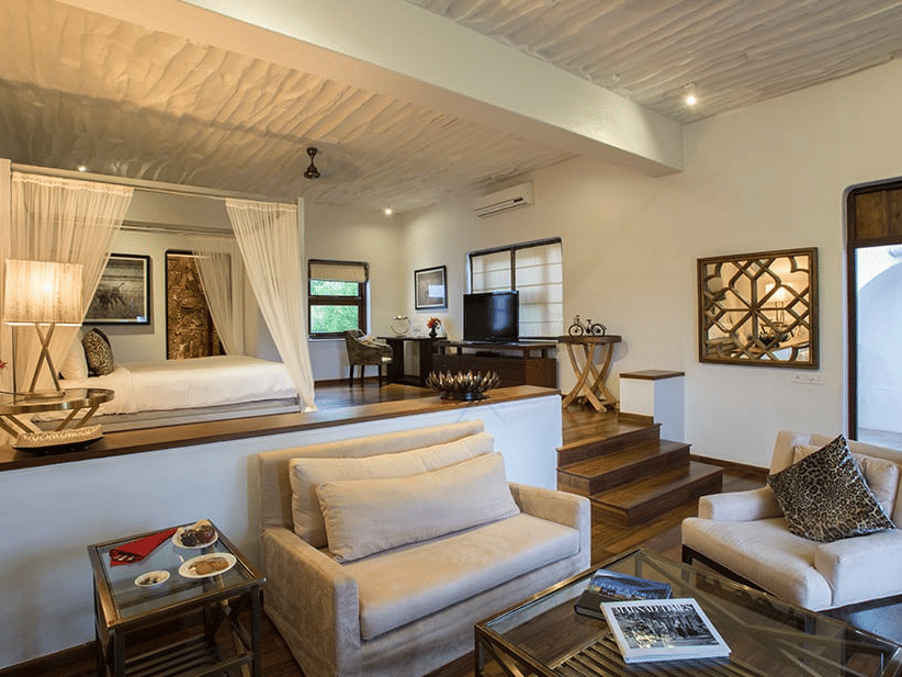 Interior of The Residence at The Serai Bandipur, featuring living space with sofas, table, wall art, and an elevated bed.