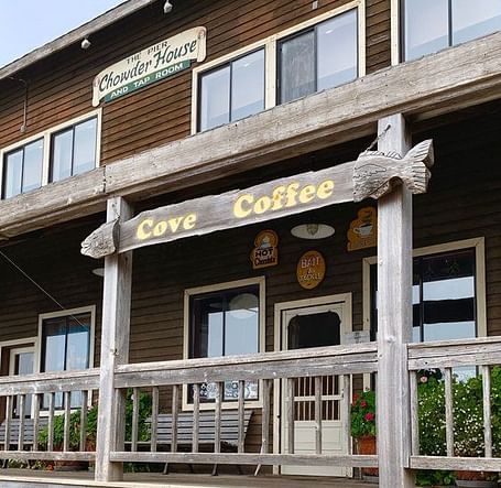 A building with multiple windows features a sign reading Cave Coffee over a covered porch with a railing.