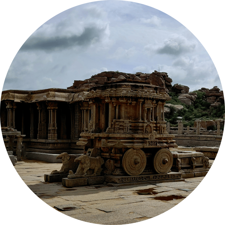 Weathered stone temple ruins in Hampi, one of the popular travelling places in Karnataka, stand across a vast courtyard, reflecting exquisite ancient craftsmanship amid boulder-strewn landscapes and cloudy skies overhead.