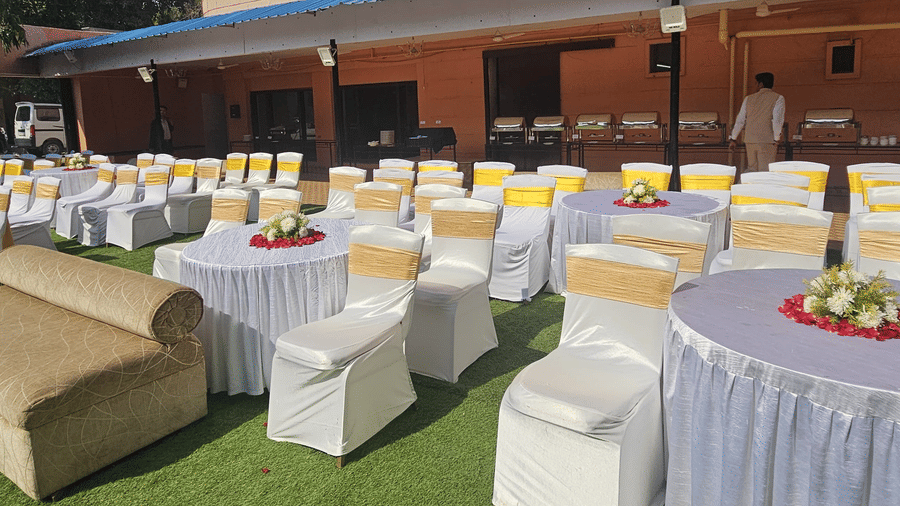 An outdoor area with round tables covered in white cloths and chairs with yellow bows on a lawn | HHI Varanasi