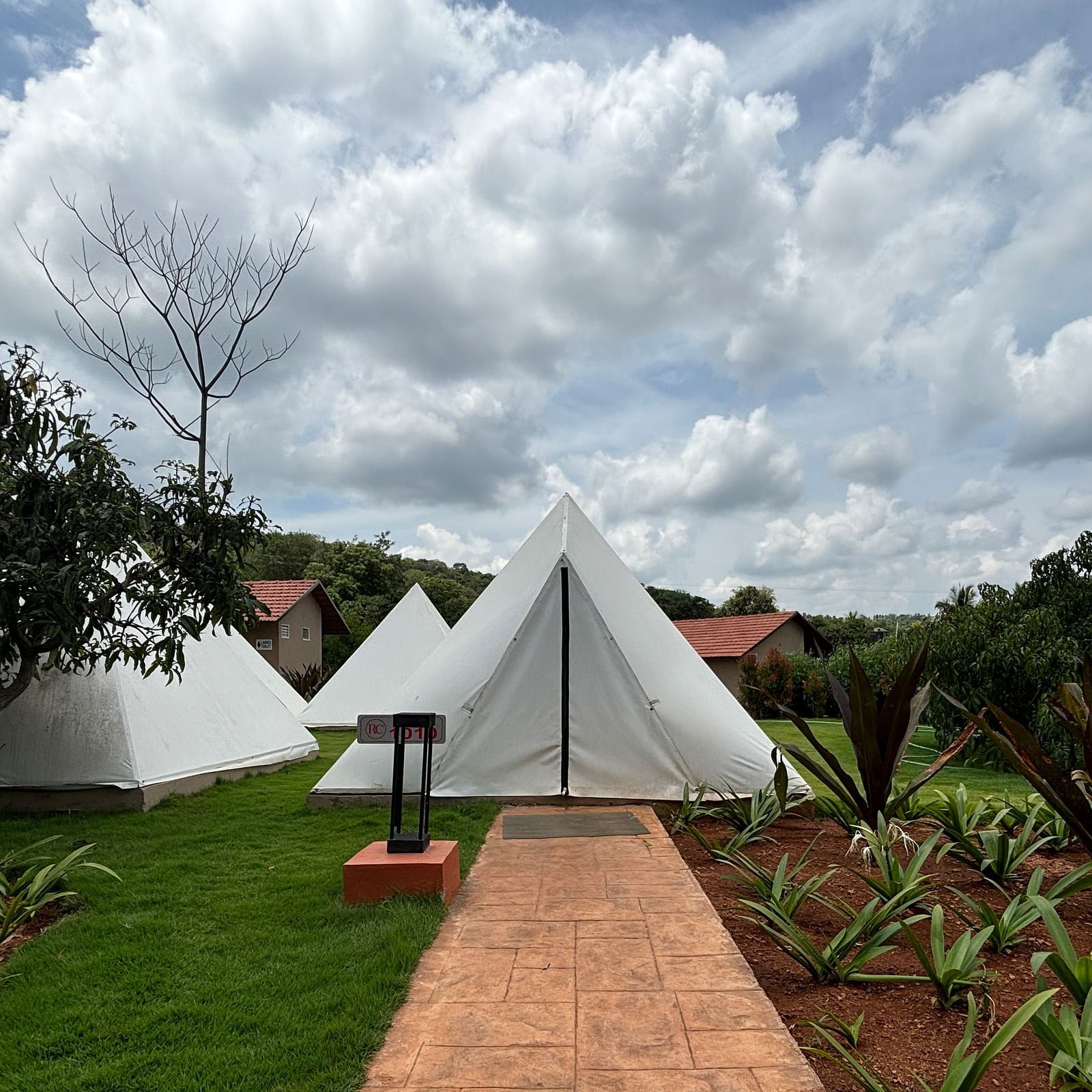 A scenic view of a resort area with tents lined along a neat walkway, surrounded by a well-maintained lawn.