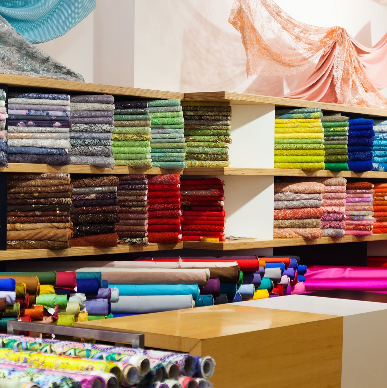 Fabric store showcasing neatly stacked colourful rolls of textiles on shelves and counters, with vibrant patterns and materials on display.