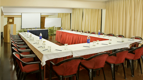 U shaped seating inside the Mantara Conference Hall with red chairs, a projector screen, a white board and curtains covering the windows at VITS Kamats Resort, Silvassa.