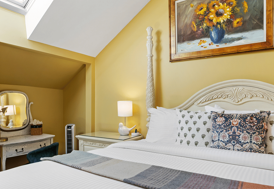 A brightly lit hotel room with a white bed, yellow walls, and a skylight.