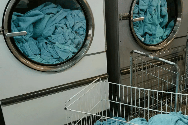 A laundry area with open washing machines and a metal basket filled with blue linen.