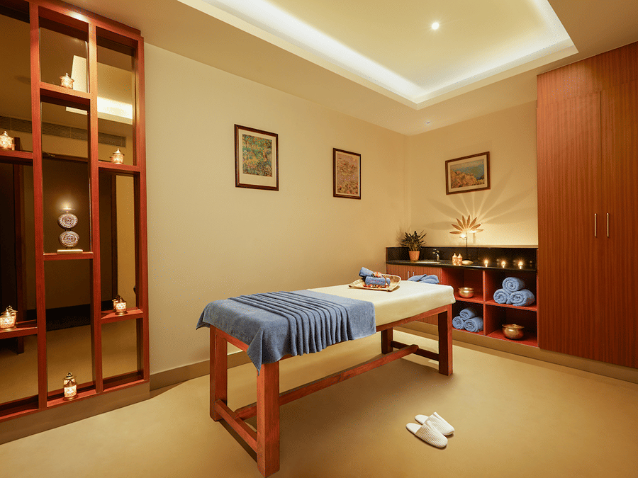 Spa room with a massage table, folded cloth, red partition, and storage cabinets - Karur 