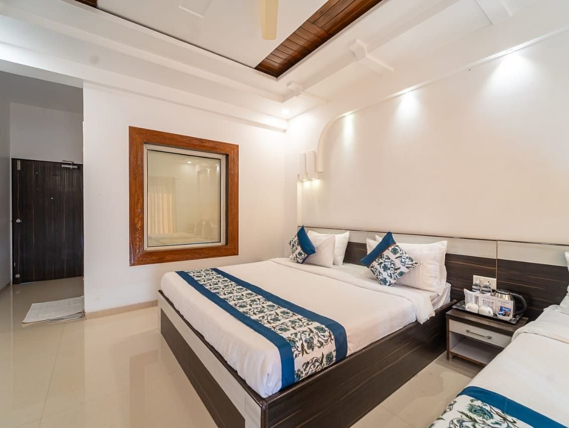 Deluxe Valley View Room featuring neatly made bed with white and blue accents, a side table, and a decorative wall mirror, under warm lighting.