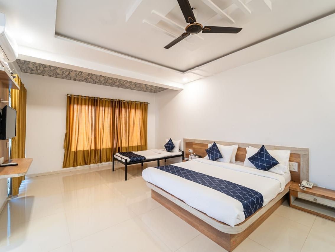 Penthouse Suite with Balcony featuring a king size bed with white linens and a gray accent runner, two blue decorative pillows, bedside tables, a mattress, and a ceiling fan.