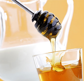 An image featuring a jug of milk and a bowl of honey placed in front of the milk jug.