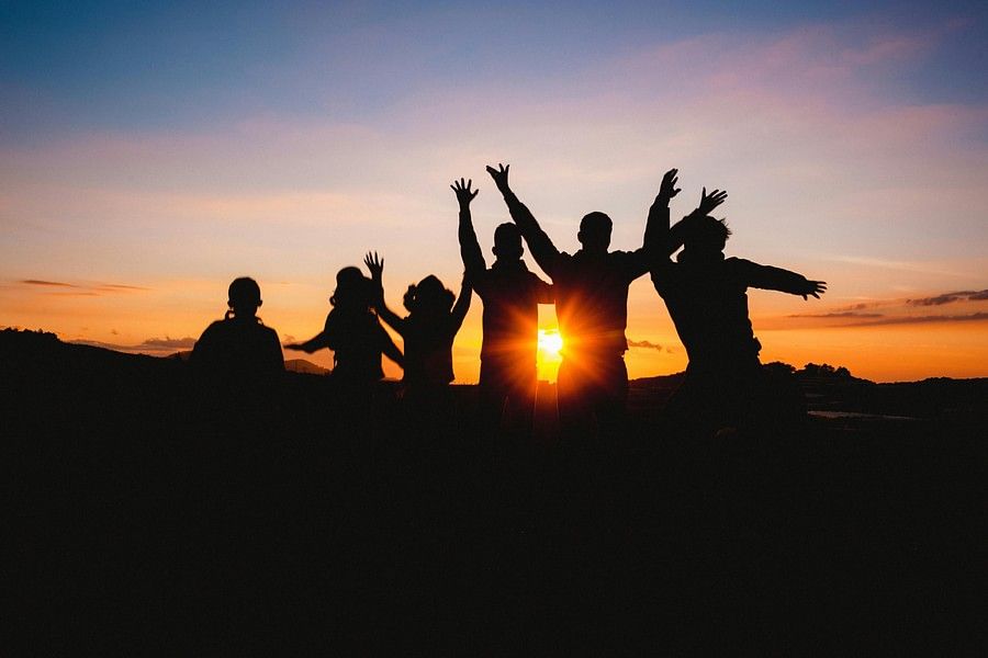 Silhouette of a group of people with raised arms, celebrating or posing against a vibrant sunset, creating a joyful atmosphere against a colorful sky.