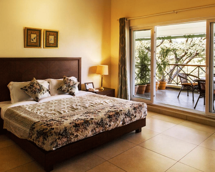 Side angle view of super deluxe room that showcases soft hues of yellow and white along with a balcony overlooking tea gardens - Lamrin Norwood Green, Palampur