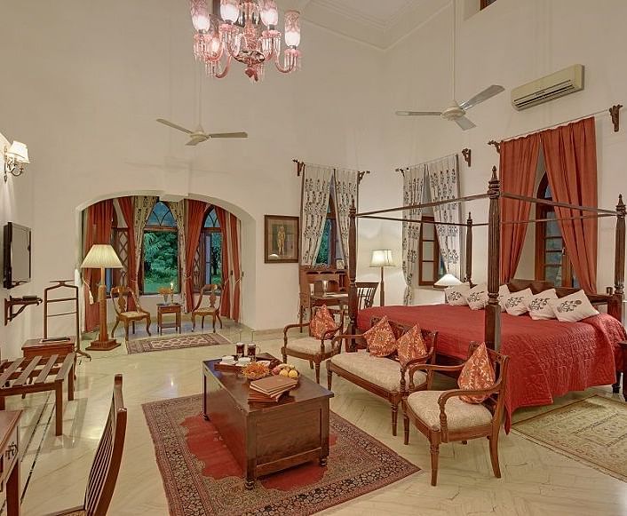 A well-appointed room with a four-poster bed, seating area, and decorative rugs, featuring arched windows and a chandelier- Shahpura Bagh.