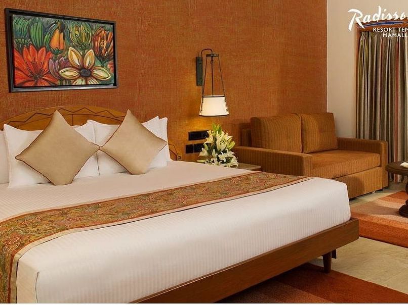 An image of a beautiful room with a bed, chairs, lamp and a wall art hanging in the background.