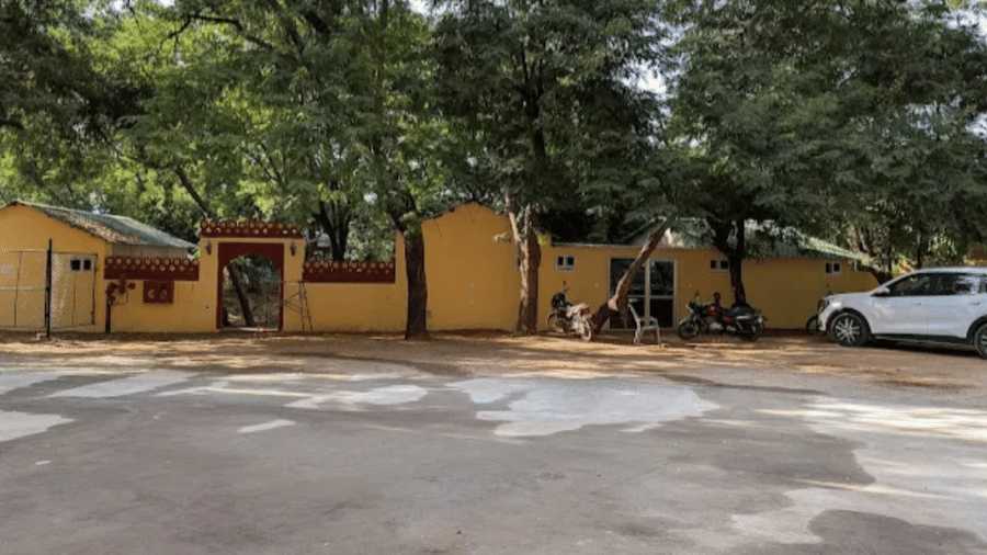 An outdoor paved area at Estherea Bagh, Ranthambore, bordered by a wall and dense trees, with a car parked to the side.