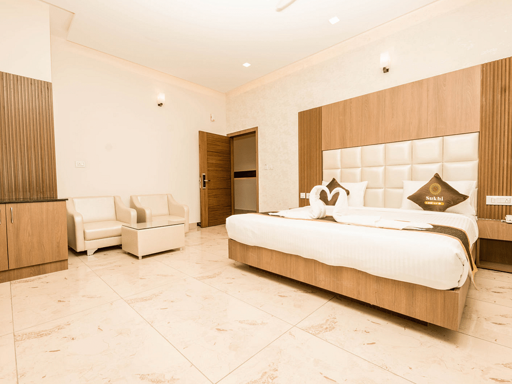 Deluxe Room With Balcony featuring a king size bed, seating area, and wooden furnishings.- Sukhi - A Luxury Stay Inn, Chikkamagaluru