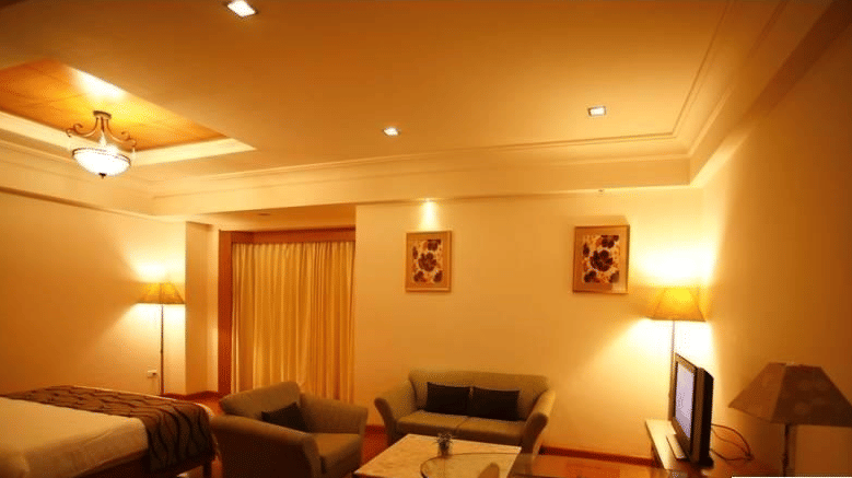 A Premium Suite at Ambrosia Sarovar Portico, Haridwar, with a large bed, seating area, a TV, coffee table, and curtains dividing the sleeping and living spaces.