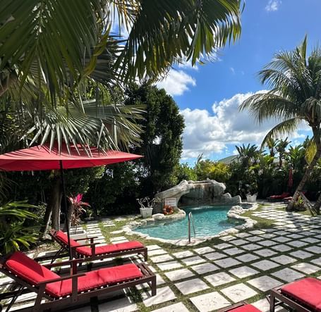 Poolside seating with red lounge chairs and umbrellas surrounded by palm trees | A Stone's Throw Away