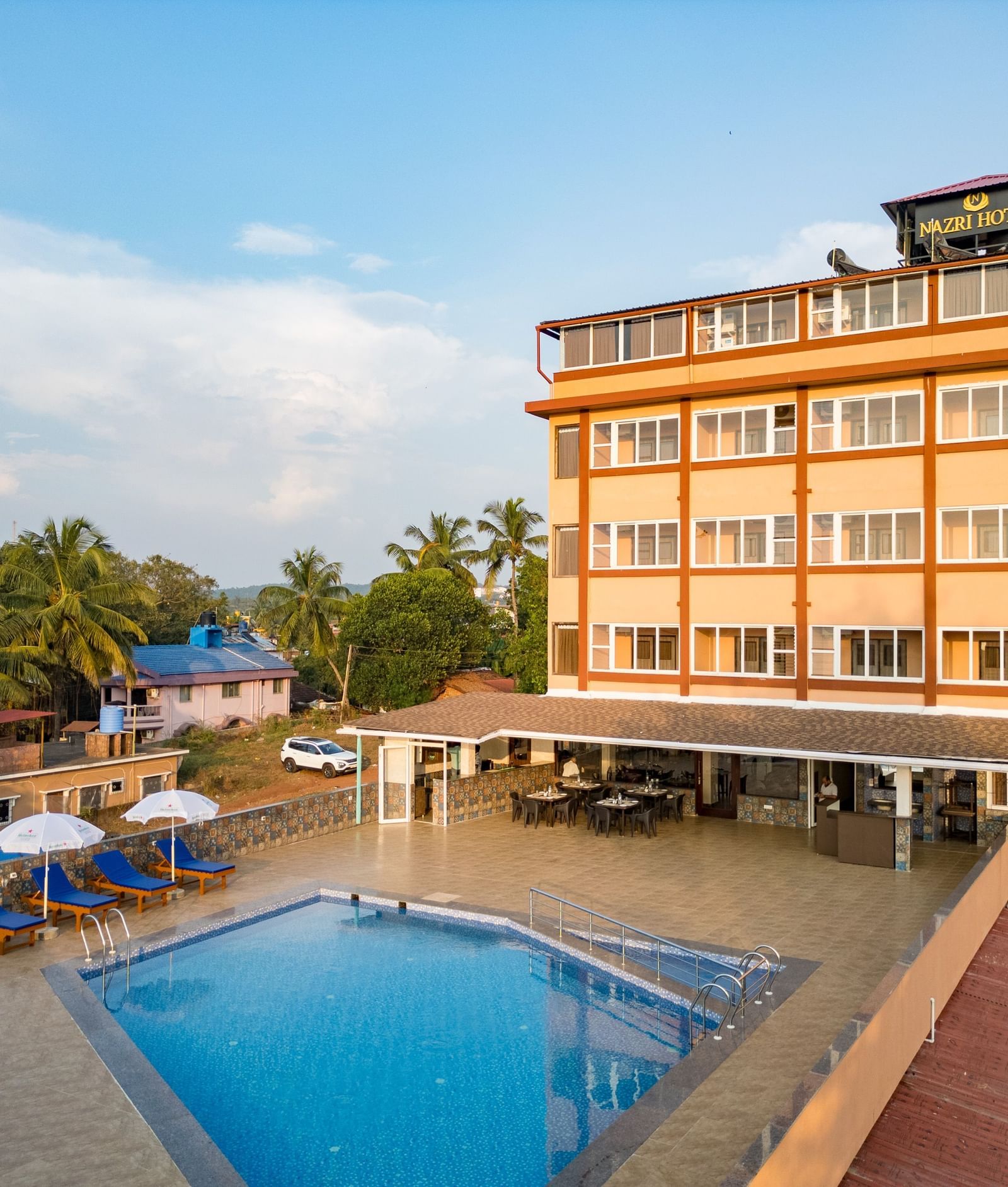 A serene view of the outdoor swimming pool surrounded by sun loungers and palm trees at Nazri The Verda, Arambol.
