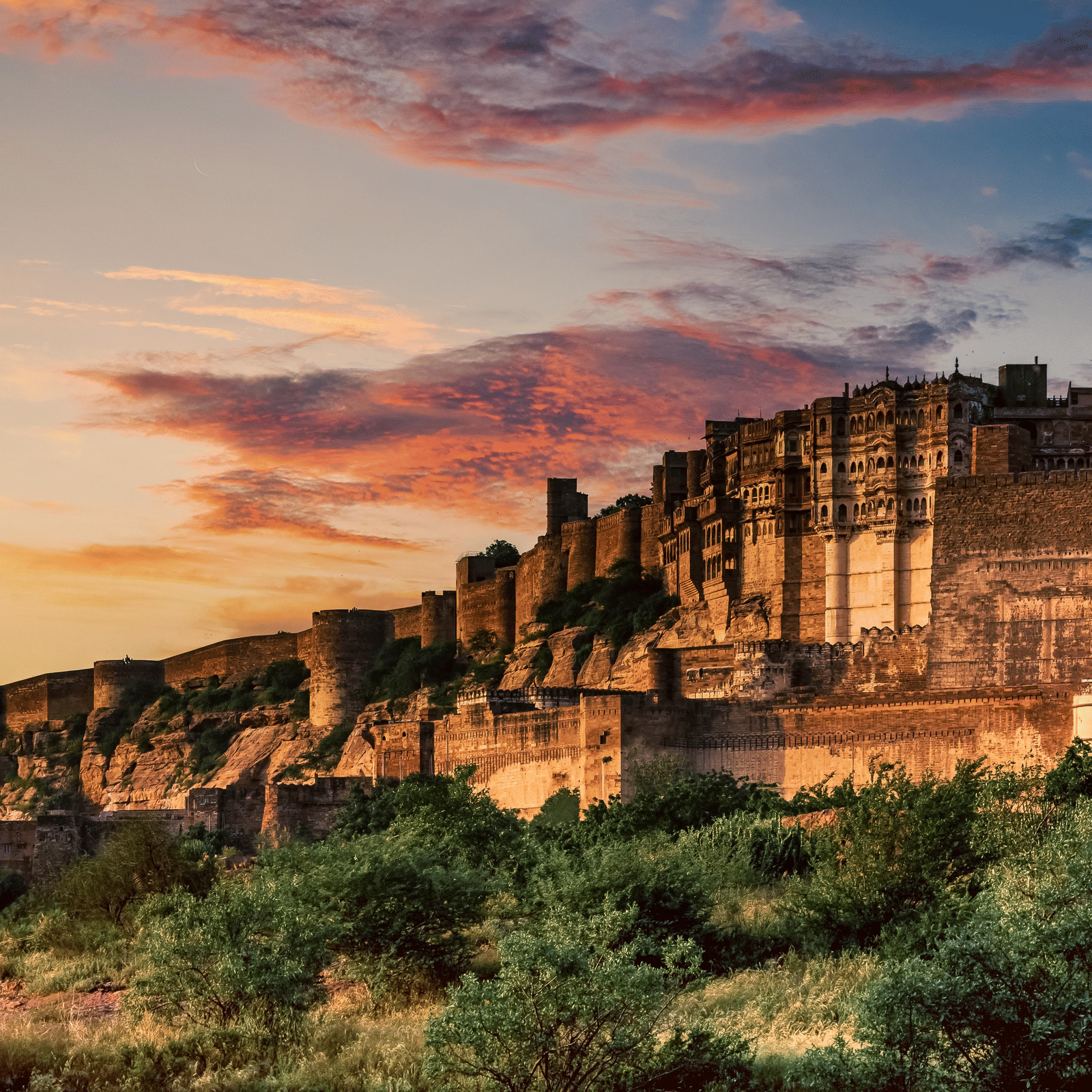 Ancient stone fort bathed in golden sunset light, with lush greenery in the foreground and colorful clouds in the sky.