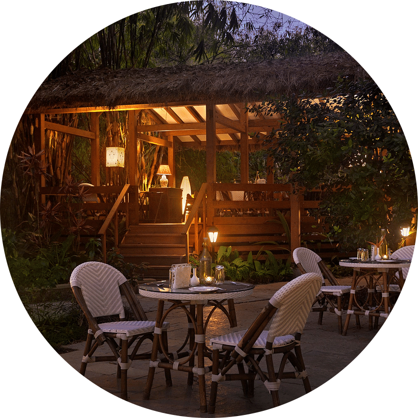 Night view of an outdoor dining area with chairs around tables and a cabin in the background.