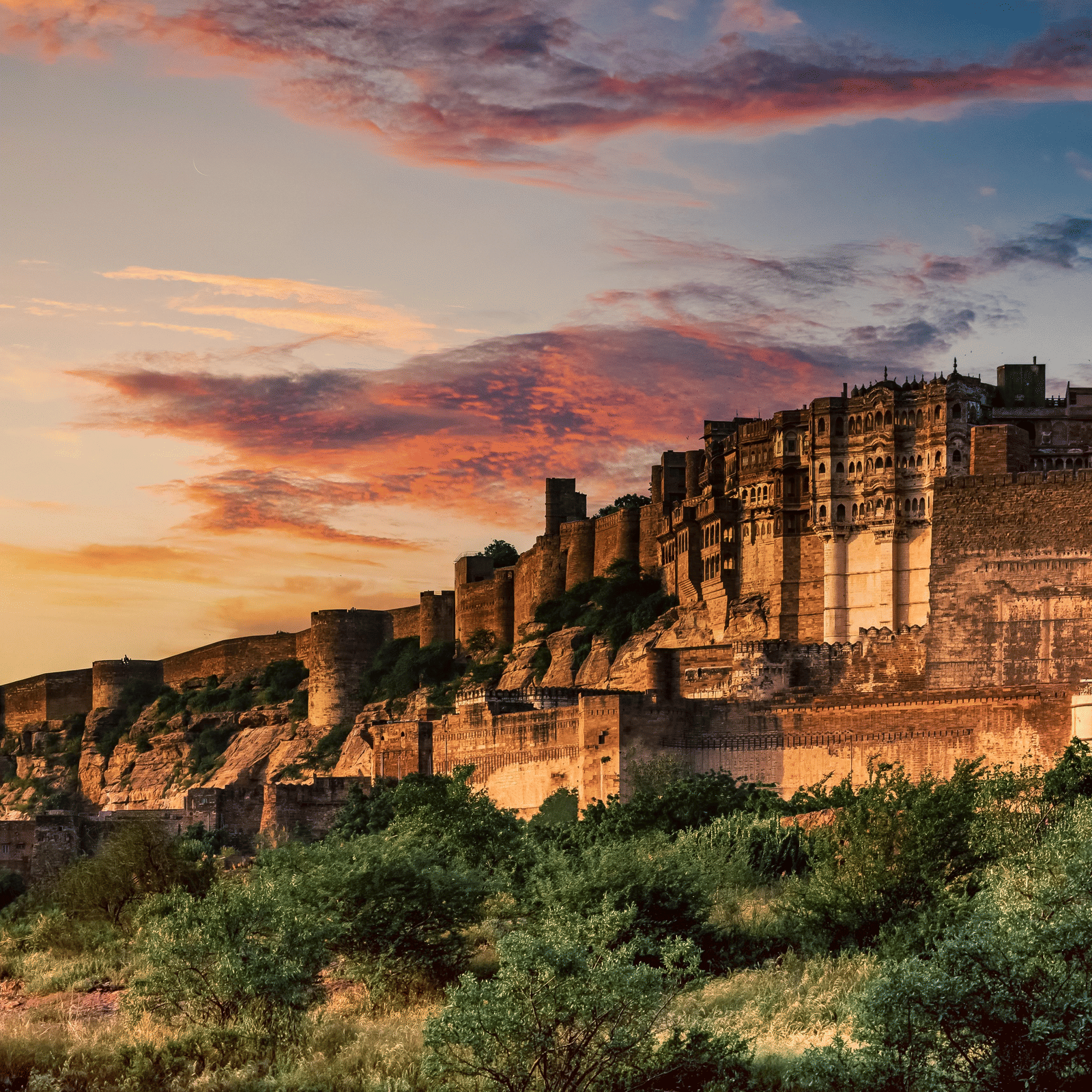 Ancient stone fort bathed in golden sunset light, with lush greenery in the foreground and colorful clouds in the sky.