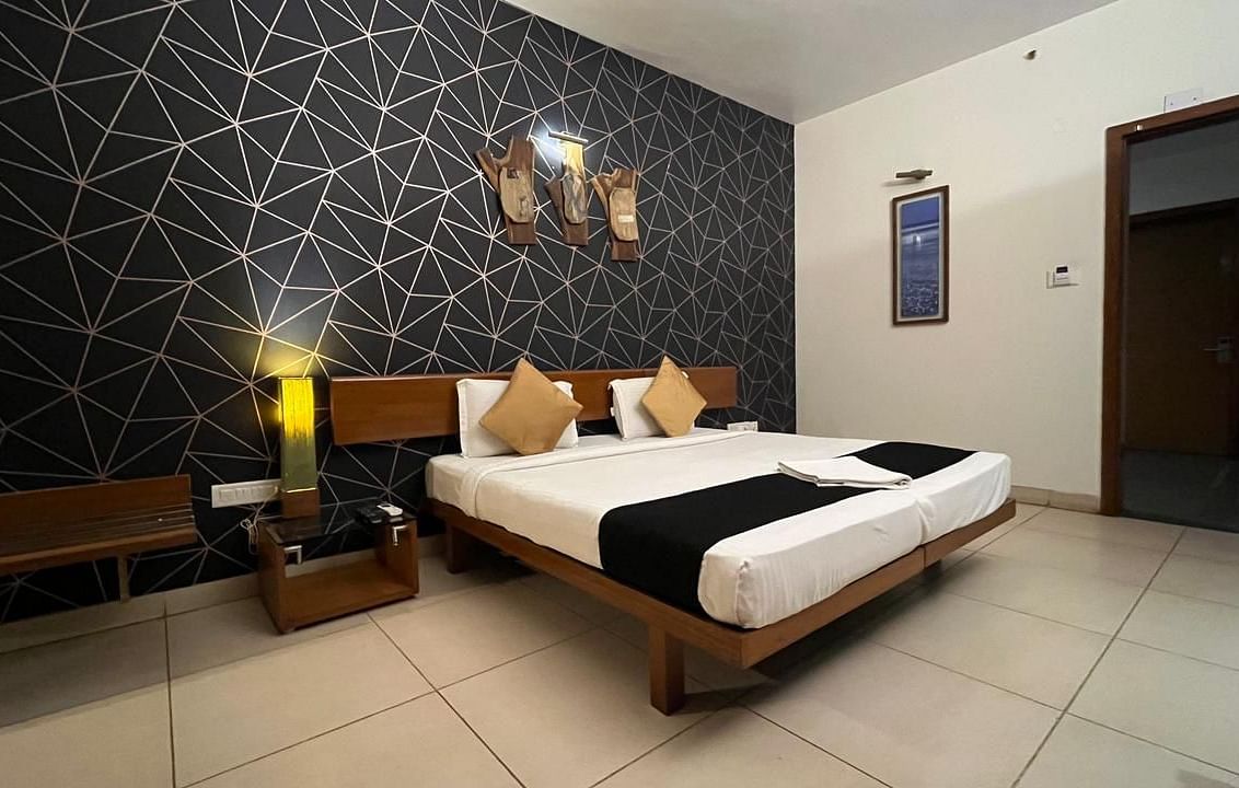 Hotel room showcasing a striking contrast between the crisp white linens of the bed and the bold, geometric pattern of the dark accent wall, complemented by warm lighting from the bedside lamps - Astra Hotels & Suites, Spice Garden Layout