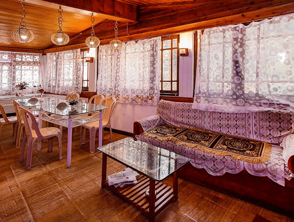 Restaurant/dining room with lace curtains, wooden walls and ceiling, glass tables, and light-coloured chairs at Hotel Dolphin Darjeeling.