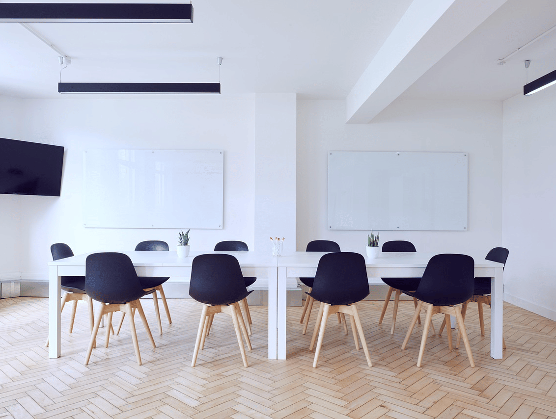 A meeting room with chairs arranged around a table with 2 whiteboards in the background.