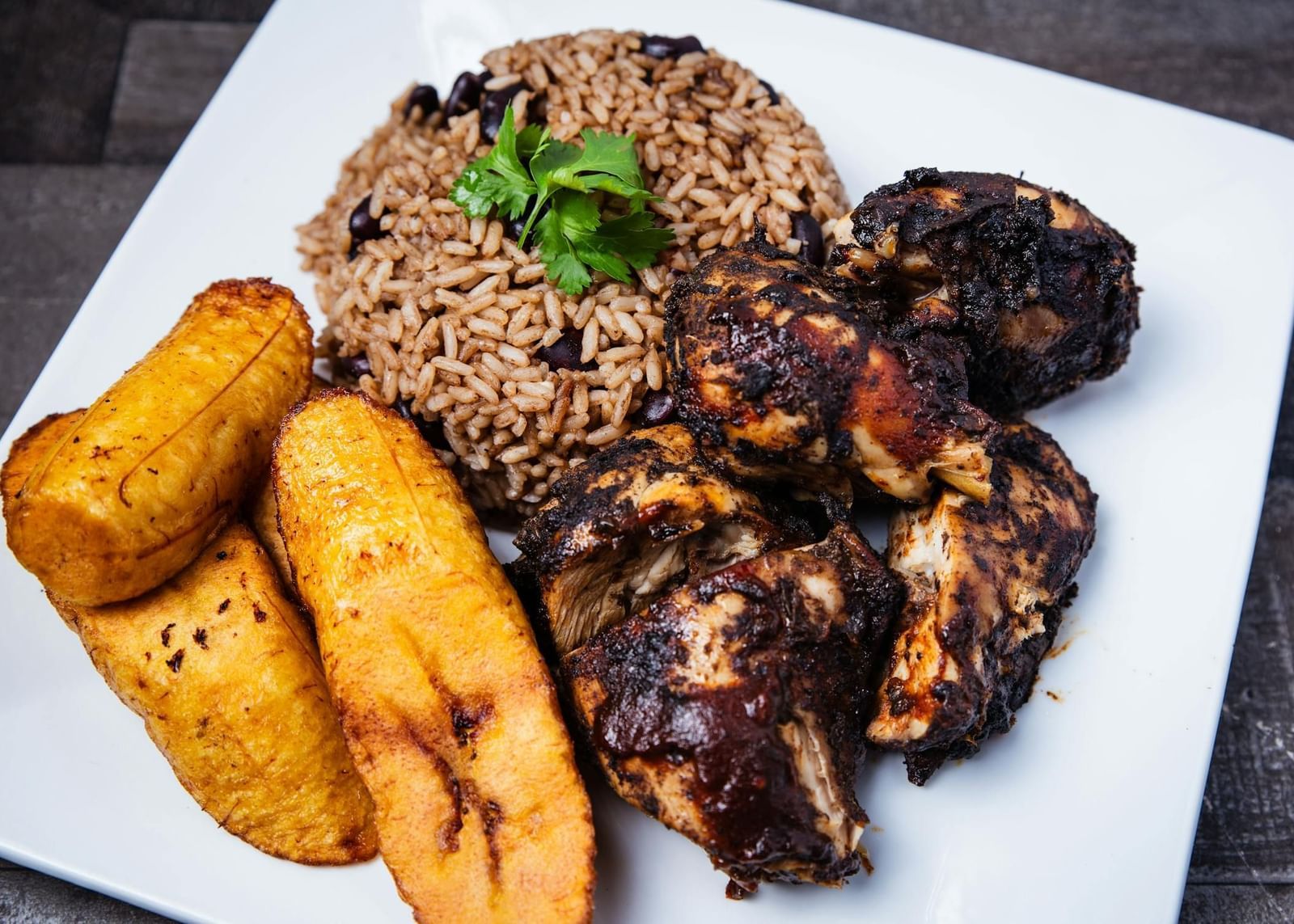 A plate with cooked chicken pieces, rice, beans, and plantains, presented as a meal at a Restaurant in Montego Bay.