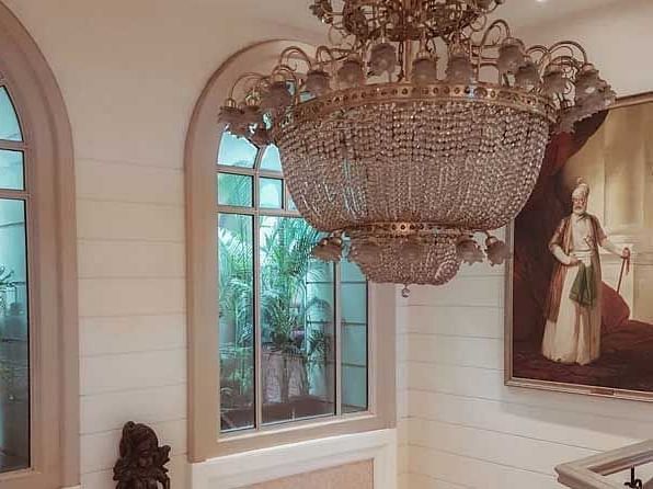 A beautiful room with a chandelier and big dome shaped windows and a potrait on the wall in the background.