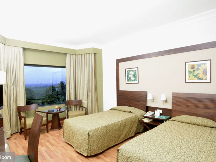 A bedroom with twin beds  at The Retreat Hotel and Convention Centre Madh Island Mumbai, with a table and chairs.