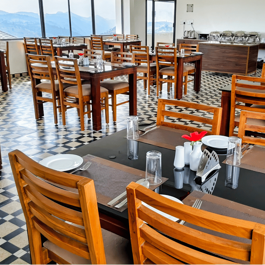 Seating arrangement inside the in-house restaurant serving the best food in Vagamon, with floor to ceiling windows in the distance having valley-views at Abad Silvermist, Vagamon