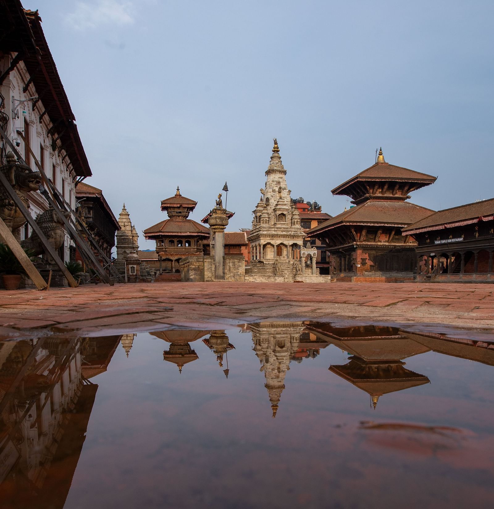 A facade view of the bhaktapur durbar square where a puddle of water is reflecting the structure