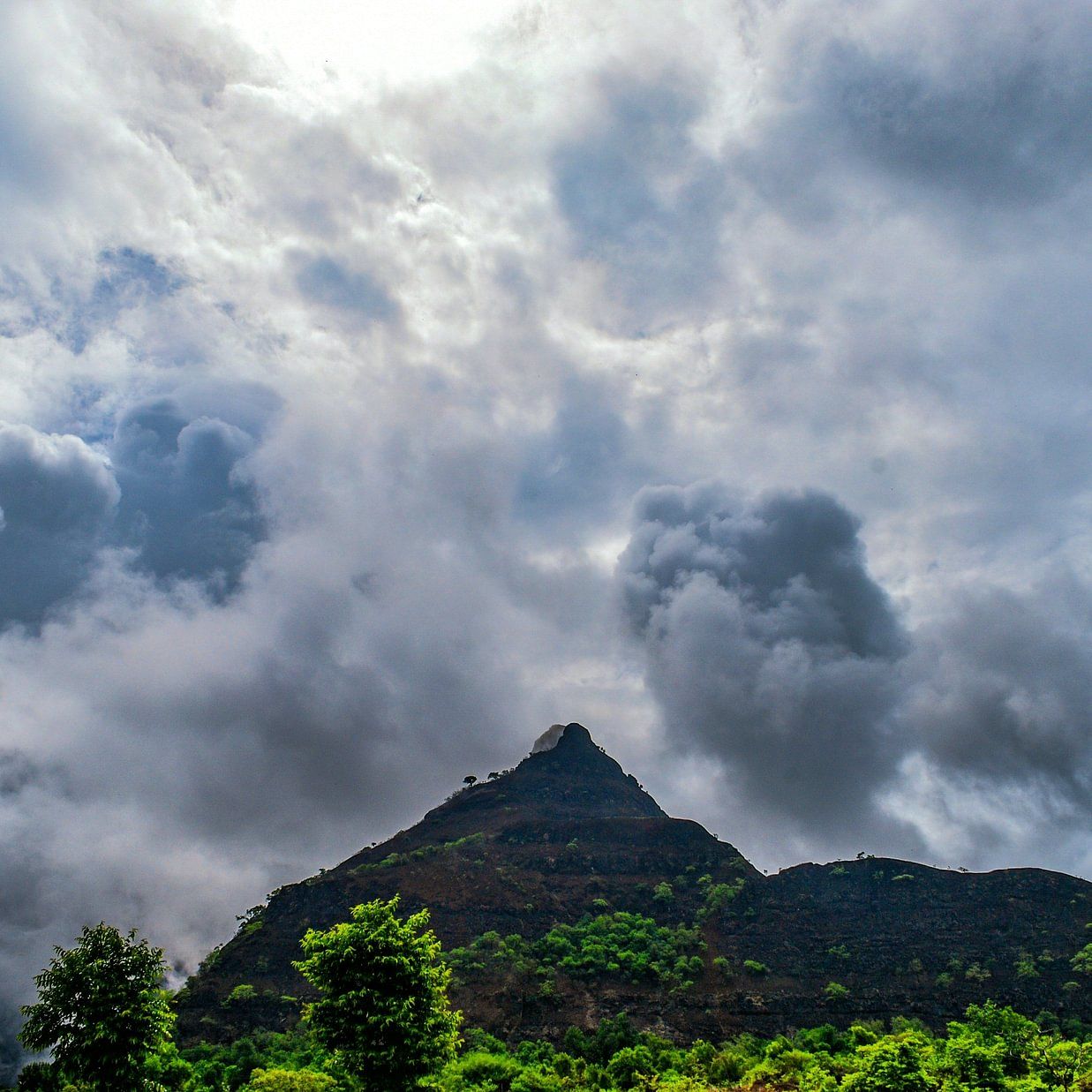 sky filled with storm clouds over a conical mountain peak.