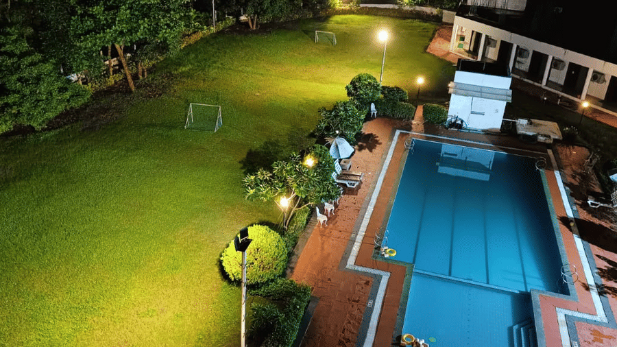 an aerial view of the lawn area next to the swimming pool as seen during the night with goal posts on the lawn and trees covering the surroundings. The lawn area is one of the best wedding venues in Silvassa at VITS Kamats Resort, Silvassa.