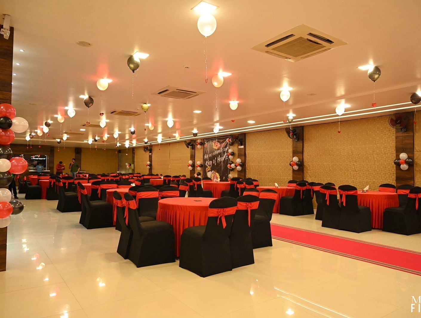 Banquet hall with red and black chair covers and ceiling lights at Mansha Regency, Port Blair.