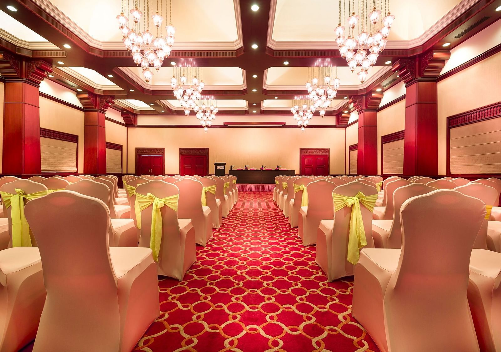 A wedding hall with white chairs tied with yellow ribbons pointing towards the stage at Grand Chennai By GRT Hotels.